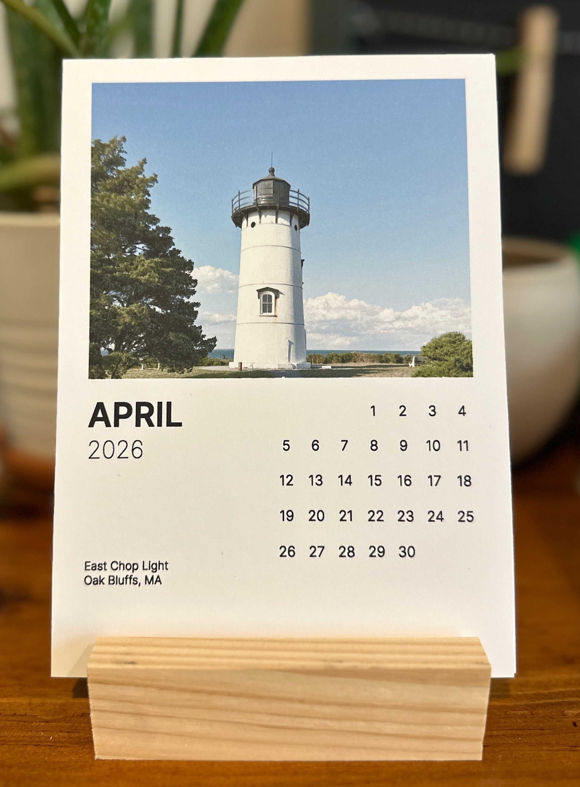 April 2026 calendar with a lighthouse image on a wooden stand.