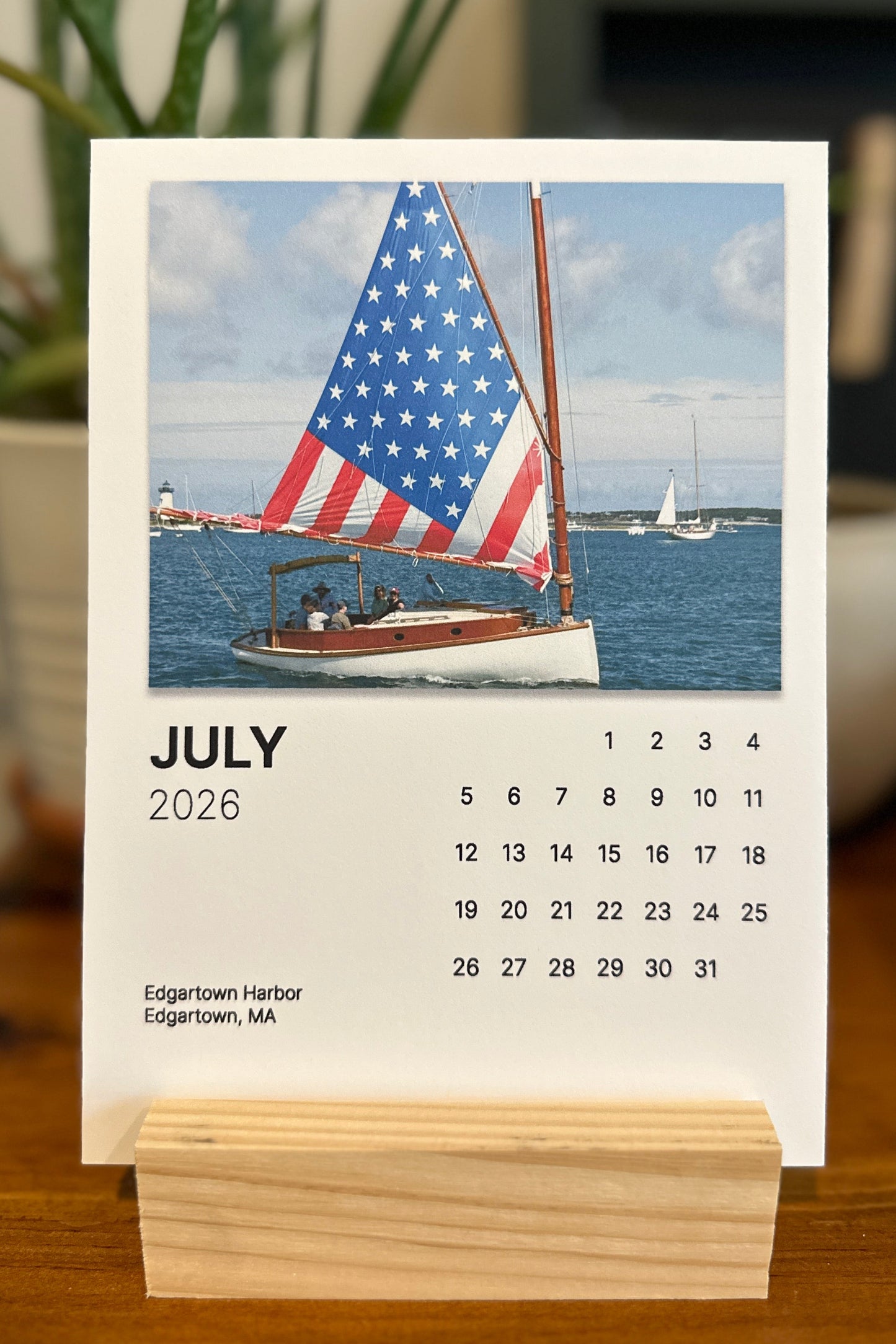 Calendar for July 2026 with a sailboat and American flag design on a wooden stand.
