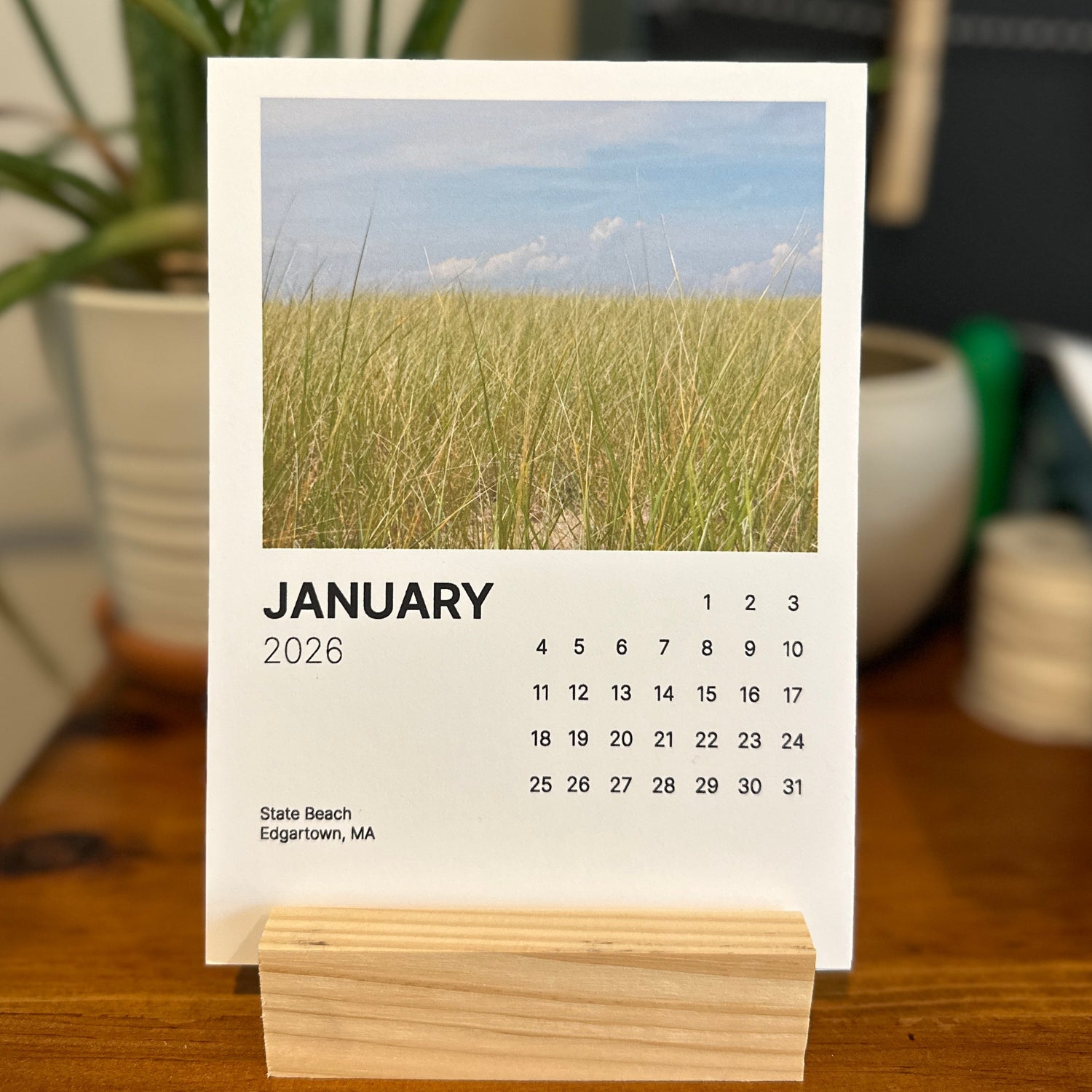 Calendar for January 2026 on a wooden stand with a grassy field background